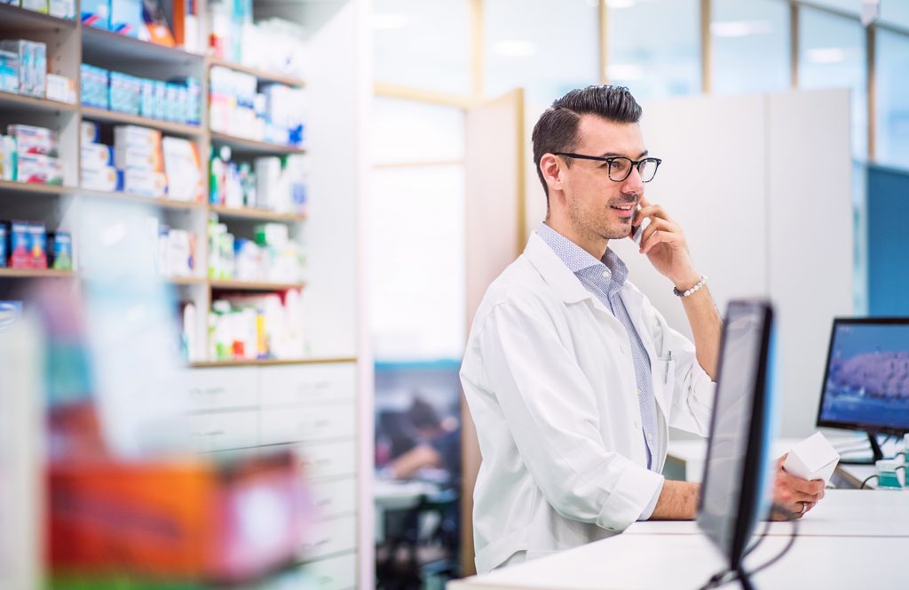 Young friendly male pharmacist with smartphone, making a phone call.