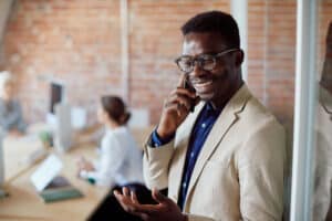 Happy black entrepreneur making phone call over teams phone while working at corporate office.