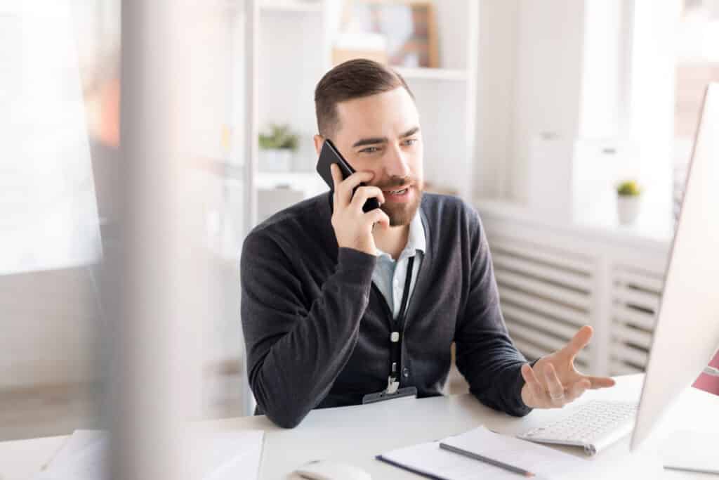 Portrait of handsome bearded businessman speaking by Teams phone while working at desk in modern office, copy space