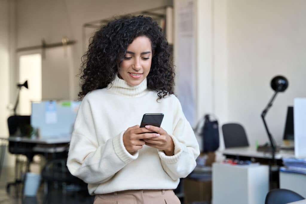 Smiling young business woman manager using teams phone standing in office