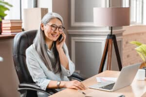 Successful mature business woman talking on teams phone at working place in office